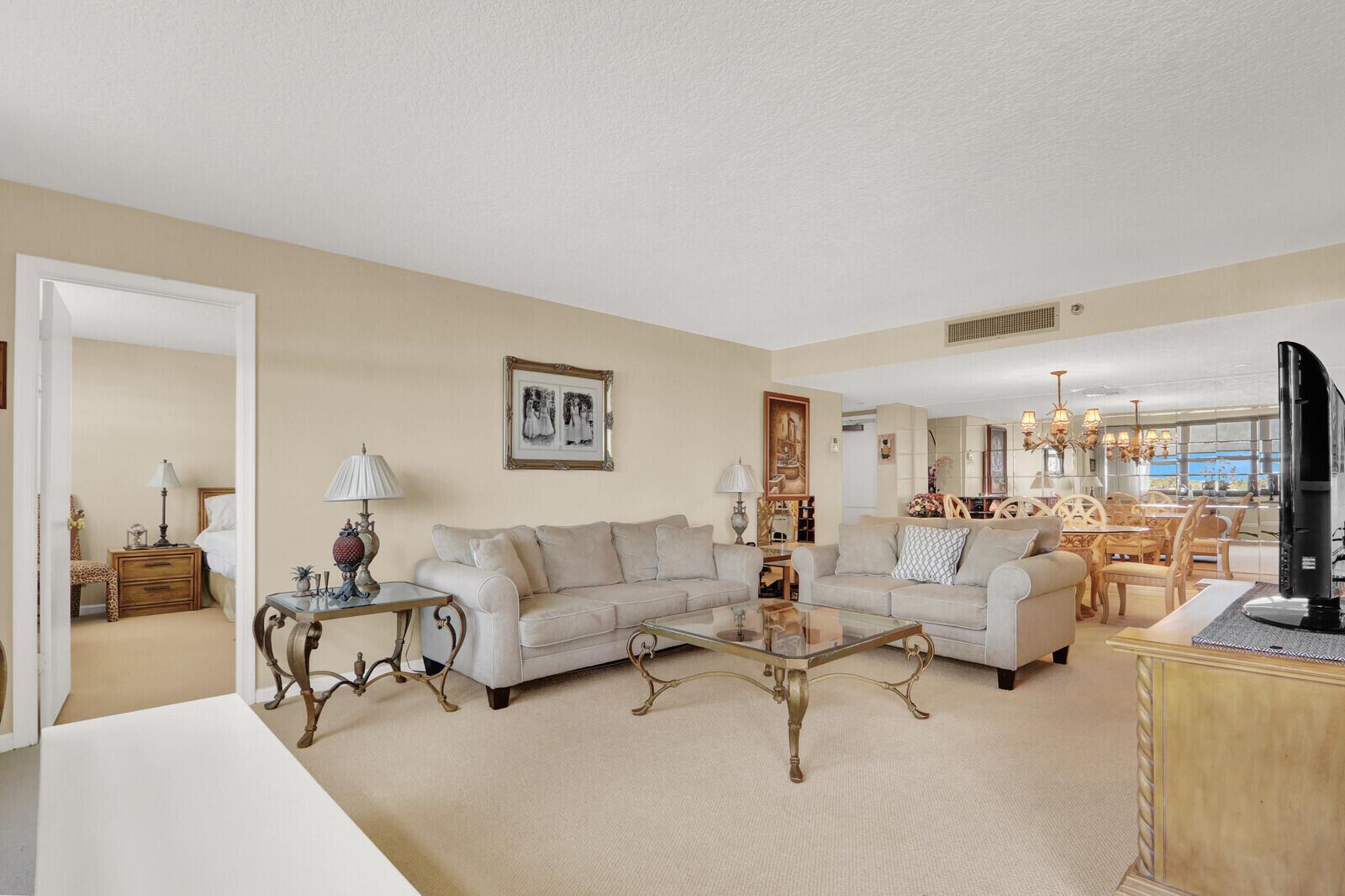 A living room with beige carpet, two light-colored sofas, and a glass-topped coffee table — 1648 Jupiter Cove Drive # 214, Jupiter FL 33469, JUPITER, FL