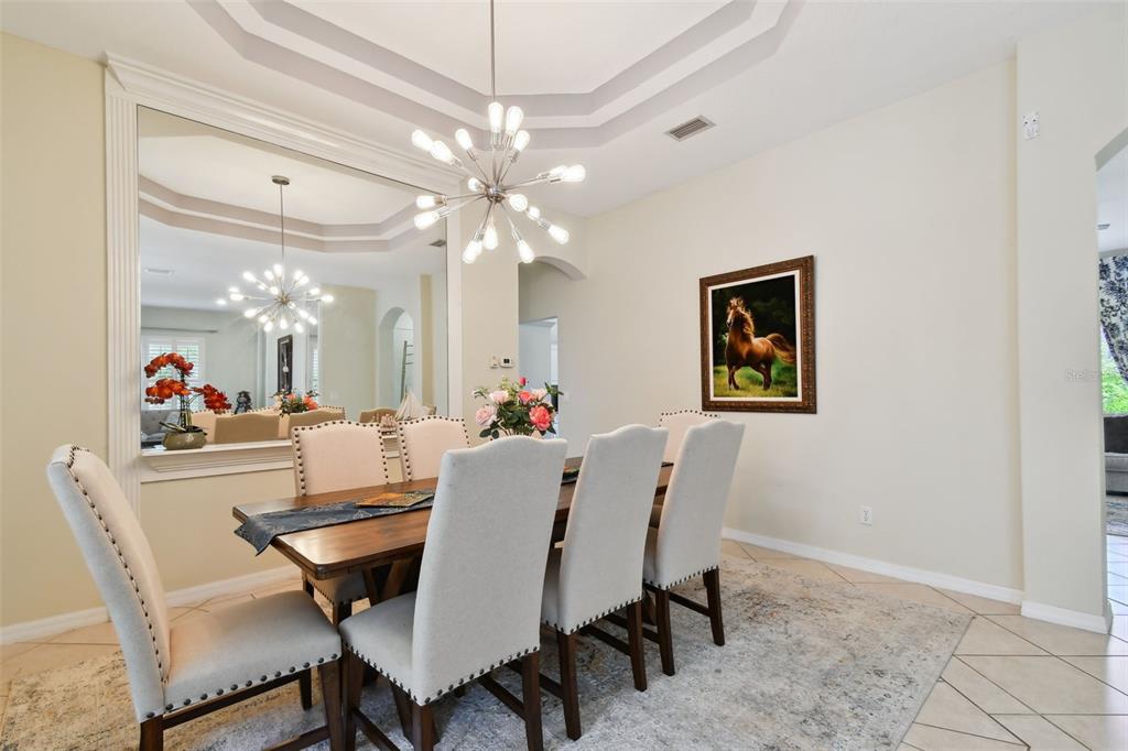 A dining room features a wooden table, upholstered chairs, a large mirror, and a chandelier — 10502 CASTLEFORD WAY, TAMPA, FL