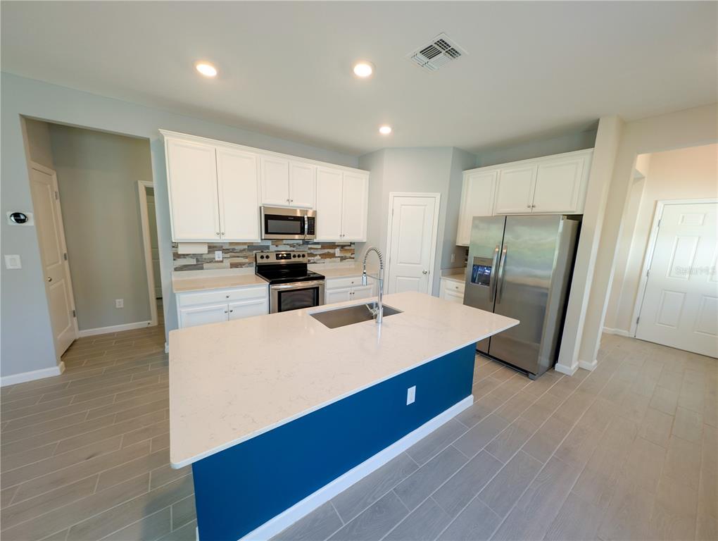A kitchen features white cabinets, a blue island with a quartz countertop, and stainless appliances — 2022 NW 44TH COURT ROAD, OCALA, FL