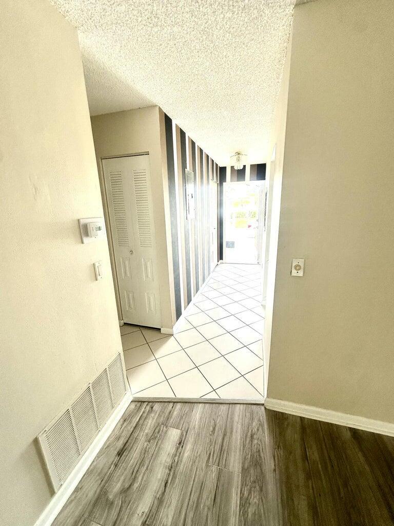 A hallway with wood-look flooring transitions to a tiled entryway featuring a striped accent wall — 6792 Moonlit Drive, Delray Beach FL 33446, DELRAY BEACH, FL