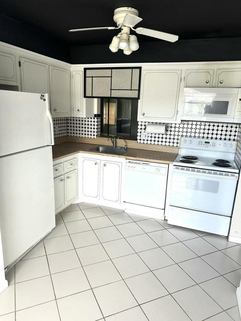 A kitchen features white cabinets, a black ceiling, a tiled backsplash, and white appliances — 6792 Moonlit Drive, Delray Beach FL 33446, DELRAY BEACH, FL