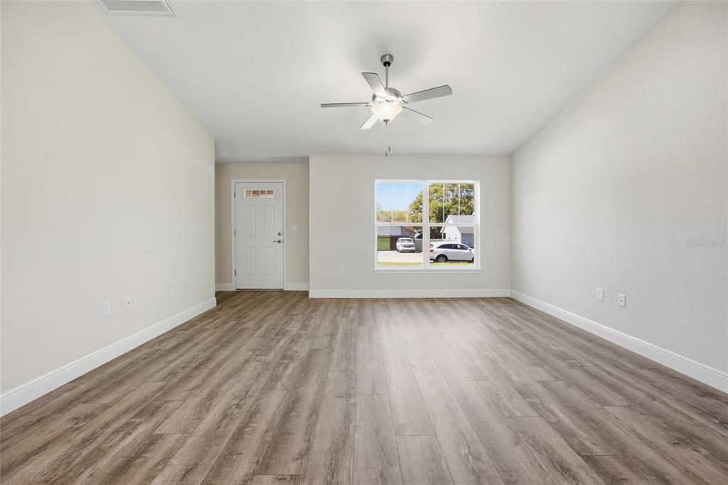An empty living room features light-colored walls, wood-look flooring, a ceiling fan, and a window — 6762 W CHERRY ROAD, OCALA, FL