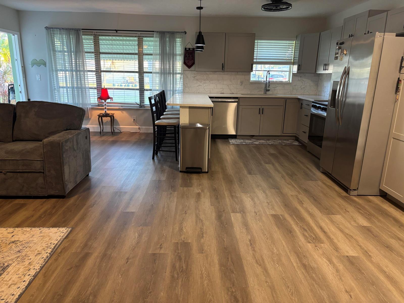 An open-concept kitchen features grey cabinets, stainless steel appliances, and wood-look flooring — 211 Country Lane # C, Boynton Beach FL 33435, BOYNTON BEACH, FL