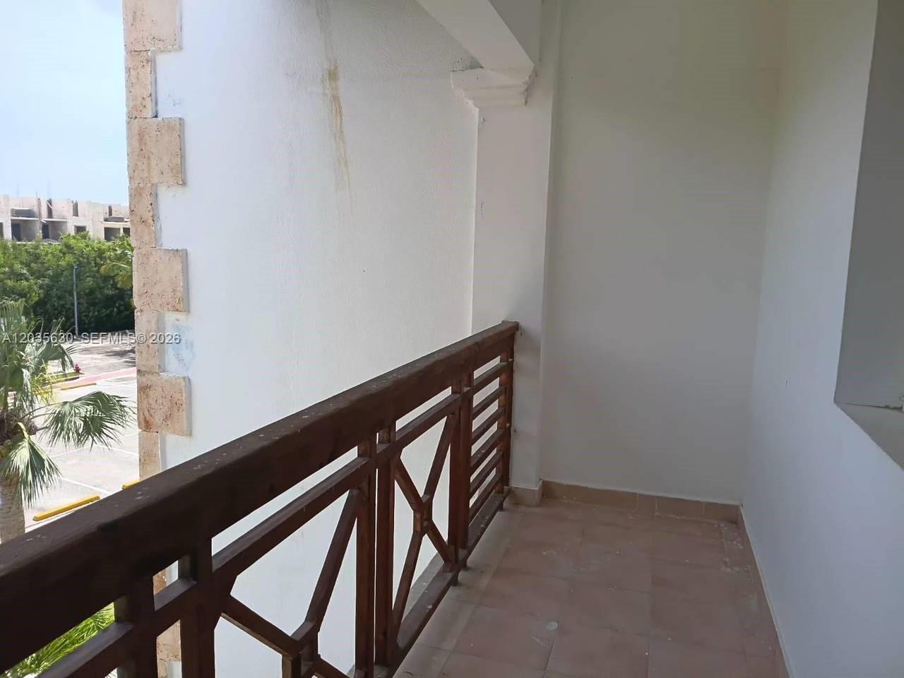 A balcony with a wooden railing overlooks a parking area and trees — 1 cap cana # 0, FL