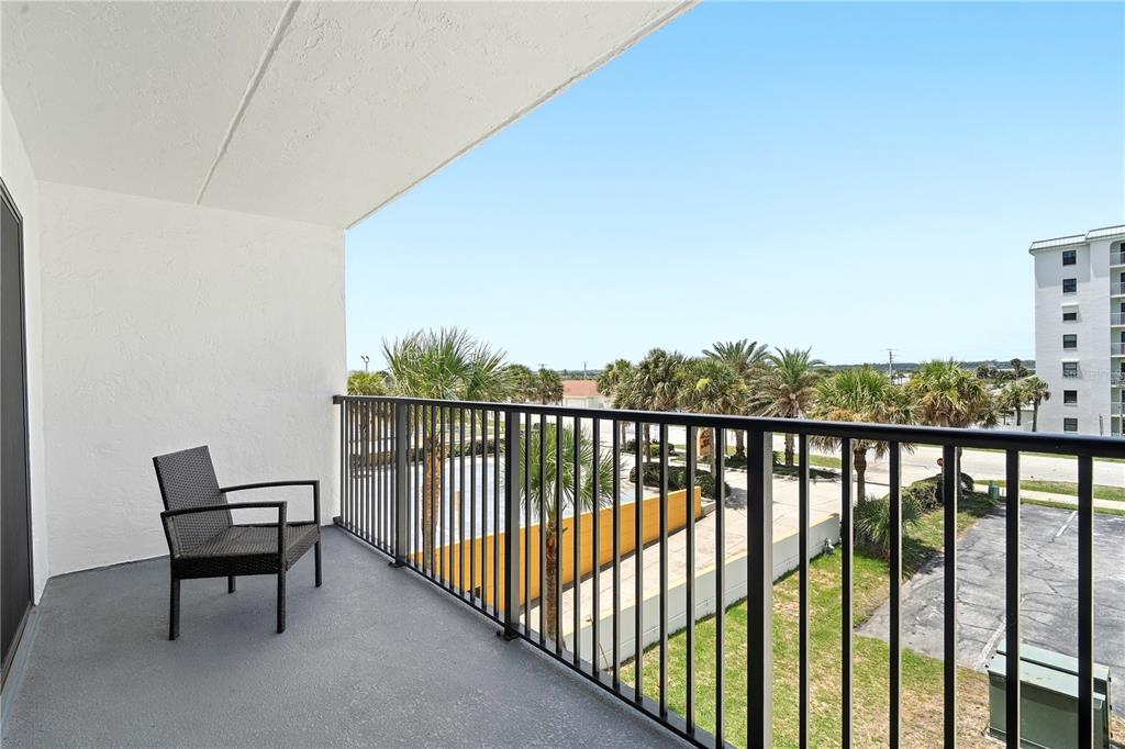 A balcony with a dark wicker chair overlooks a parking lot, palm trees, and buildings — 3807 S ATLANTIC AVENUE UNIT 4040, DAYTONA BEACH SHORES, FL