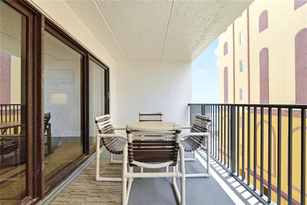 A balcony with a small table and three chairs overlooks a neighboring yellow building — 3807 S ATLANTIC AVENUE UNIT 4040, DAYTONA BEACH SHORES, FL