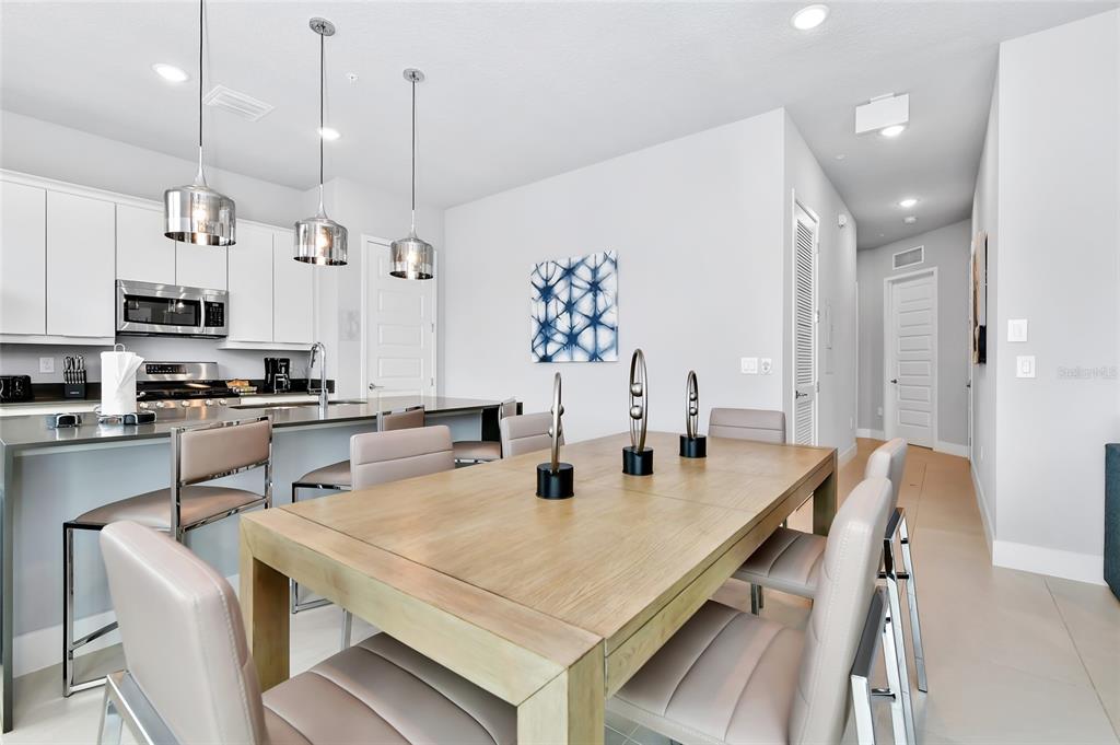A modern kitchen and dining area features white cabinets, stainless steel appliances, and light wood furniture — 7770 SANDY RIDGE DRIVE UNIT 108, KISSIMMEE, FL