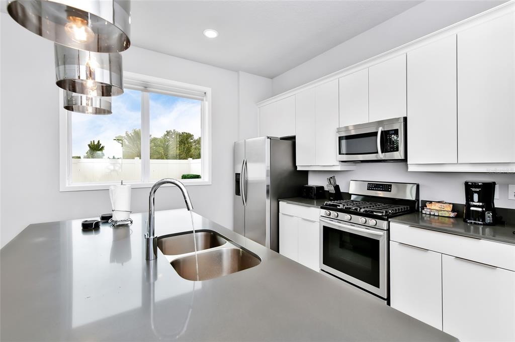 A modern kitchen features white cabinets, stainless steel appliances, and a gray quartz island countertop — 7770 SANDY RIDGE DRIVE UNIT 108, KISSIMMEE, FL