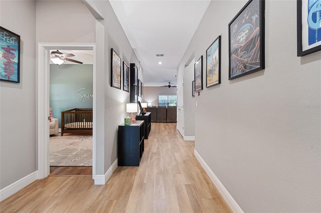 A hallway with light wood-look flooring leads to a living area and a nursery — 504 E 14TH STREET, SANFORD, FL