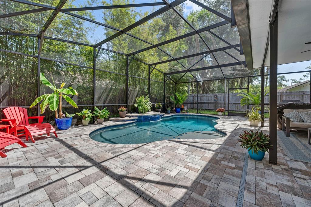 A screened-in pool patio features stone pavers, a small waterfall, and several potted plants — 504 E 14TH STREET, SANFORD, FL