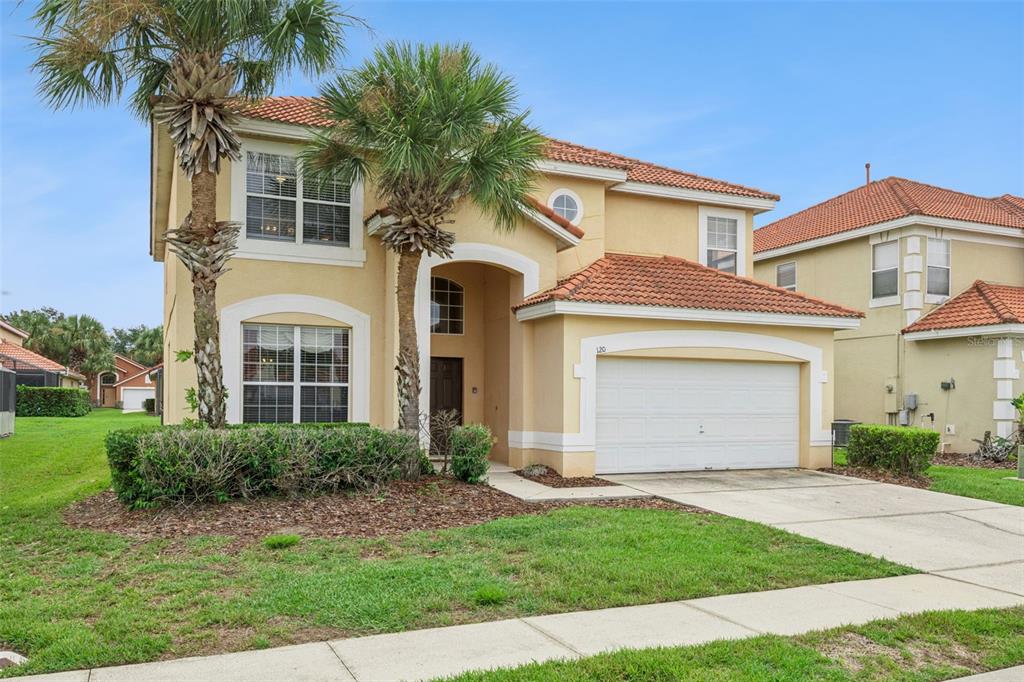A two-story stucco house with a tile roof, a two-car garage, and palm trees — 120 SARAGOSSA AVENUE, DAVENPORT, FL
