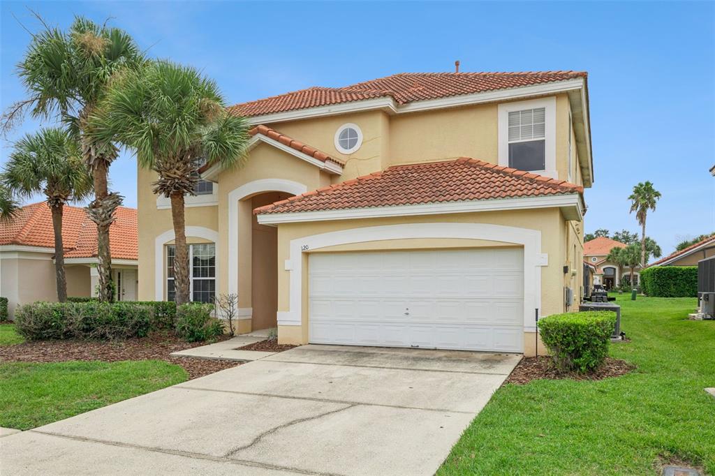 A two-story, beige stucco house with a tiled roof, a two-car garage, and palm trees — 120 SARAGOSSA AVENUE, DAVENPORT, FL