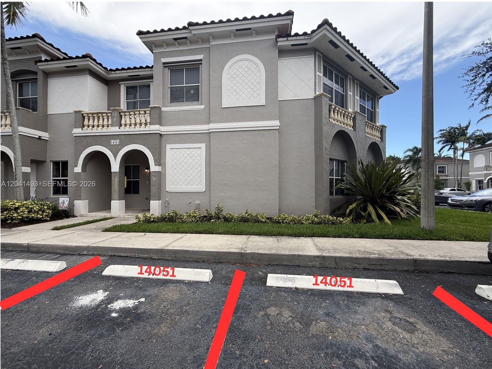 A two-story townhouse exterior features gray stucco walls, arched entryways, and two designated parking spaces — 14051 SW 49th Ct # 7, Miramar FL 33027, MIRAMAR, FL