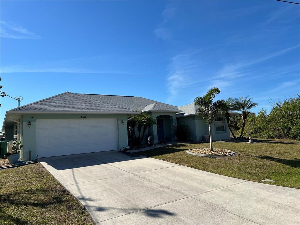 A single-story house with a light green exterior, a two-car garage, and a palm tree — 9458 MELODY CIRCLE, PORT CHARLOTTE, FL