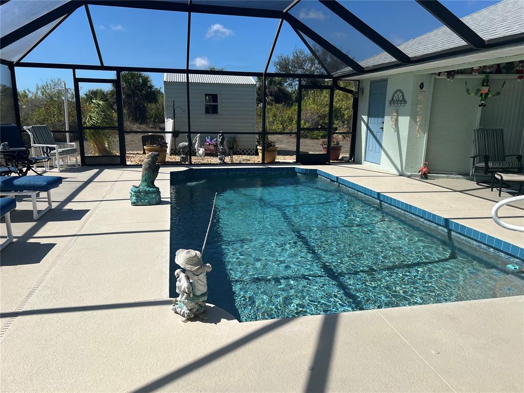 A screened-in swimming pool area features a concrete deck, patio furniture, and a storage shed — 9458 MELODY CIRCLE, PORT CHARLOTTE, FL