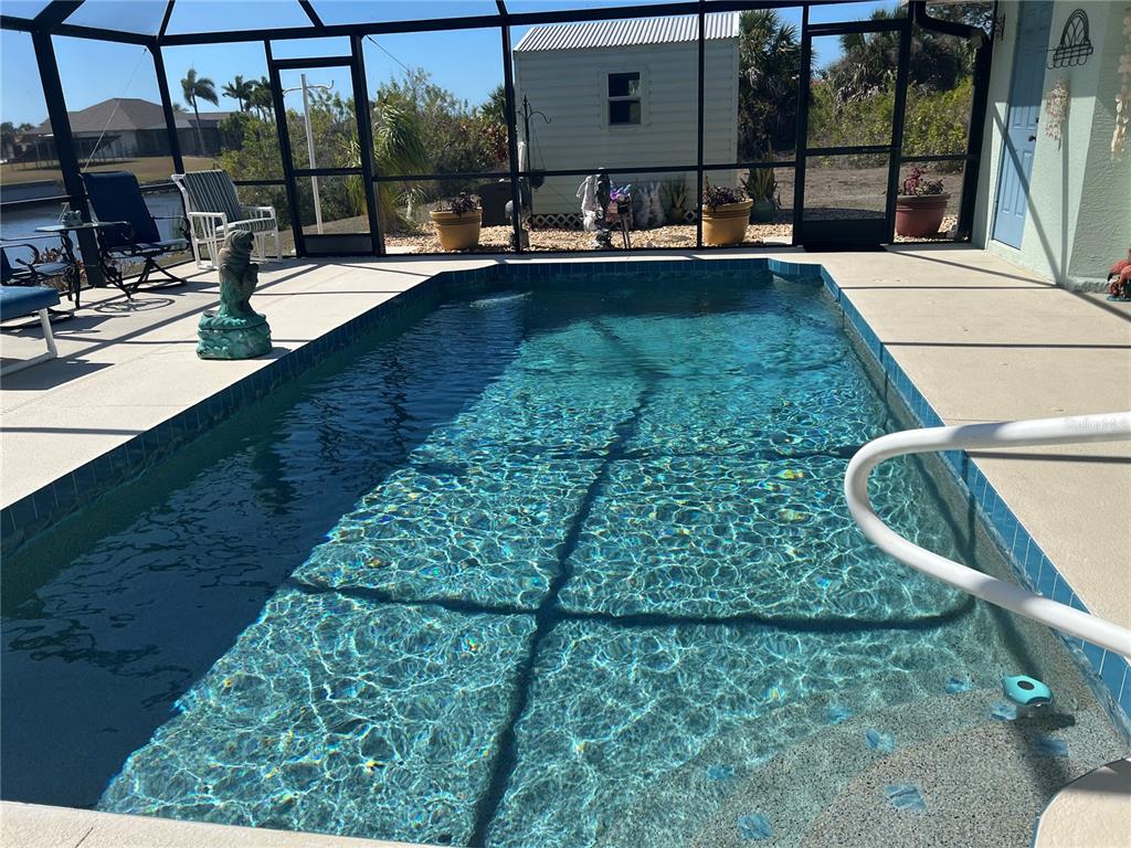 A screened-in swimming pool with a concrete deck and a small storage shed outside — 9458 MELODY CIRCLE, PORT CHARLOTTE, FL