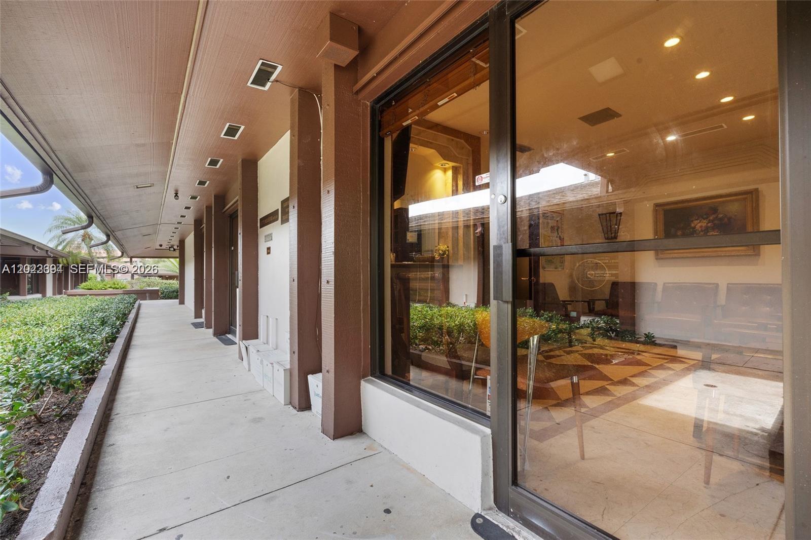 A covered outdoor walkway leads to a glass-fronted office space with interior seating — 8525 SW 92nd St # 16, Miami FL 33156, MIAMI, FL