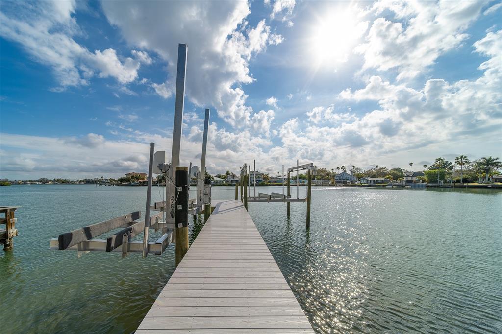 A wooden dock extends into a calm waterway featuring a boat lift under a sunny sky — 1217 BAY SHORE BOULEVARD, INDIAN ROCKS BEACH, FL
