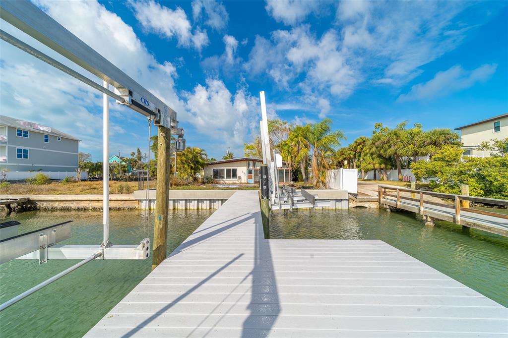 A wooden dock extends over the water toward a house with a boat lift — 1217 BAY SHORE BOULEVARD, INDIAN ROCKS BEACH, FL