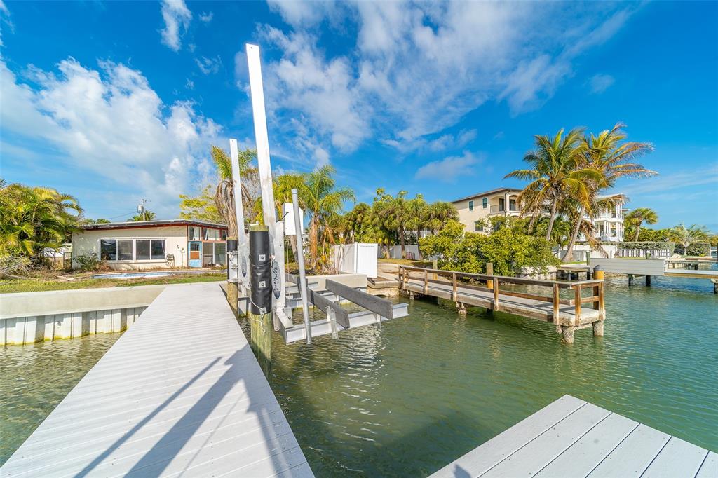 A white boat lift stands beside a wooden dock extending into a canal near houses — 1217 BAY SHORE BOULEVARD, INDIAN ROCKS BEACH, FL