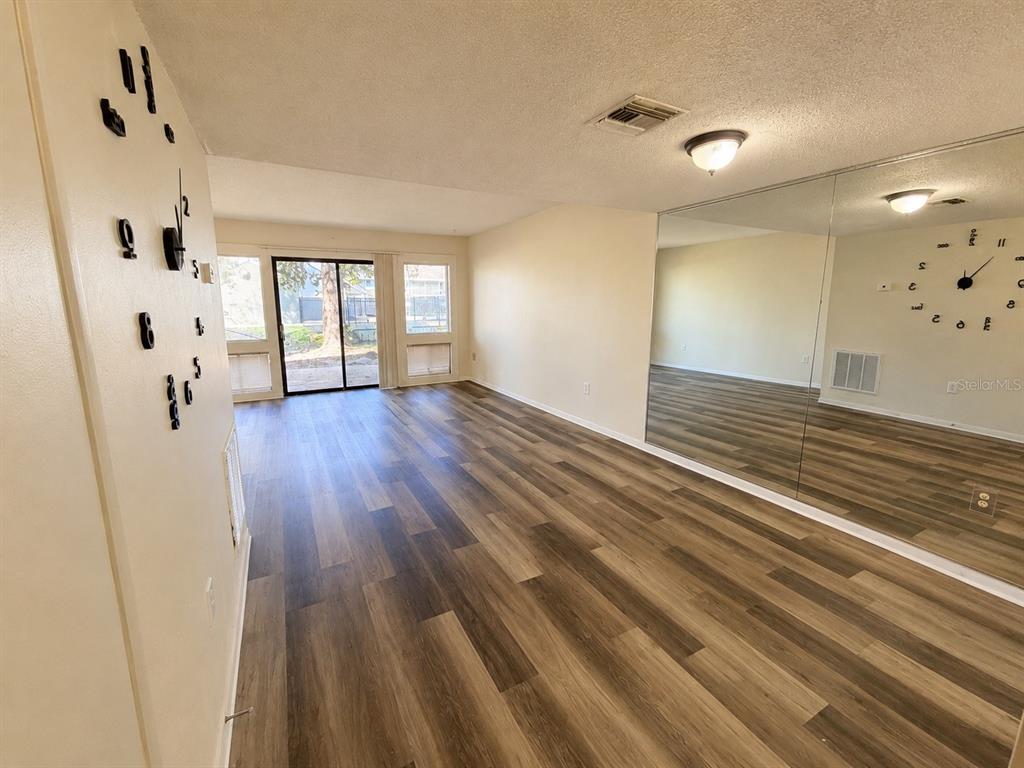 An empty living room features wood-look flooring, a mirrored wall, and a sliding glass door — 5967 WINDHOVER DRIVE UNIT 7D, ORLANDO, FL