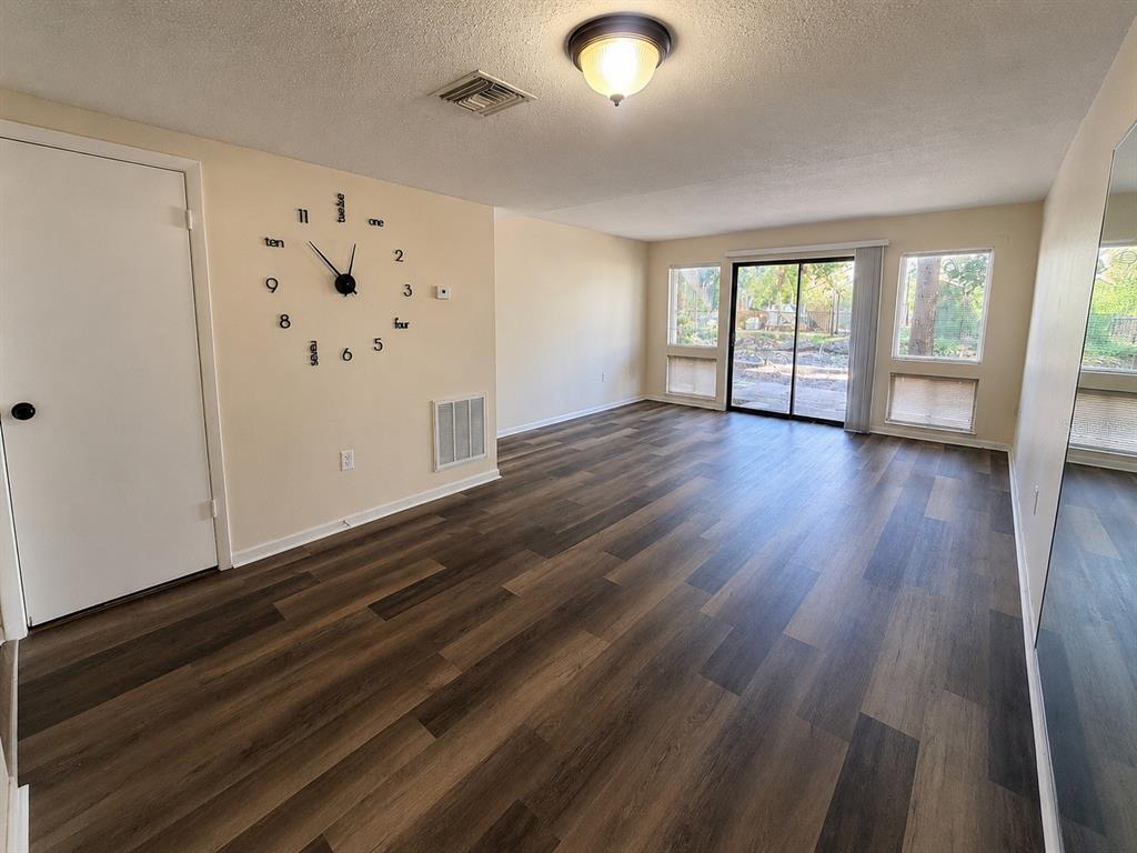 A living room features wood-look flooring, a wall-mounted clock, and a sliding glass door — 5967 WINDHOVER DRIVE UNIT 7D, ORLANDO, FL