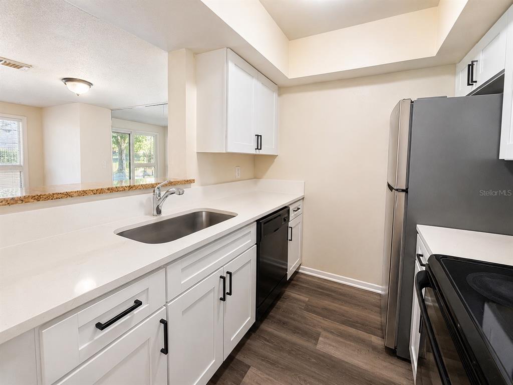 A kitchen features white cabinets, stainless steel appliances, a sink, and wood-look flooring — 5967 WINDHOVER DRIVE UNIT 7D, ORLANDO, FL