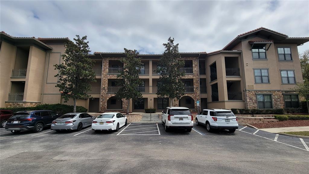 A three-story apartment building features a stone facade, balconies, and a parking lot in front — 914 CHARO PARKWAY UNIT 123, DAVENPORT, FL
