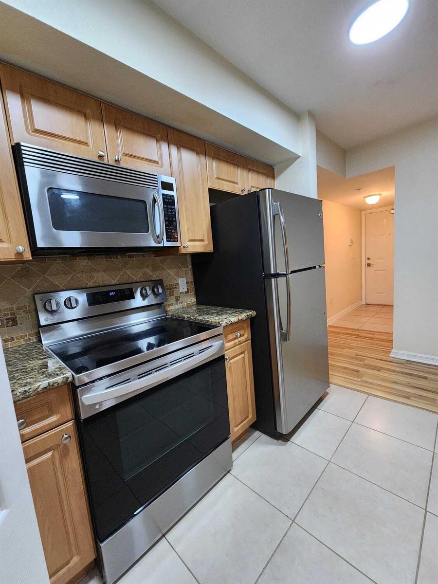 A kitchen features stainless steel appliances, wood cabinets, granite countertops, and light-colored tile flooring — 6777 Heritage # 1208, Boynton Beach FL 33437, BOYNTON BEACH, FL