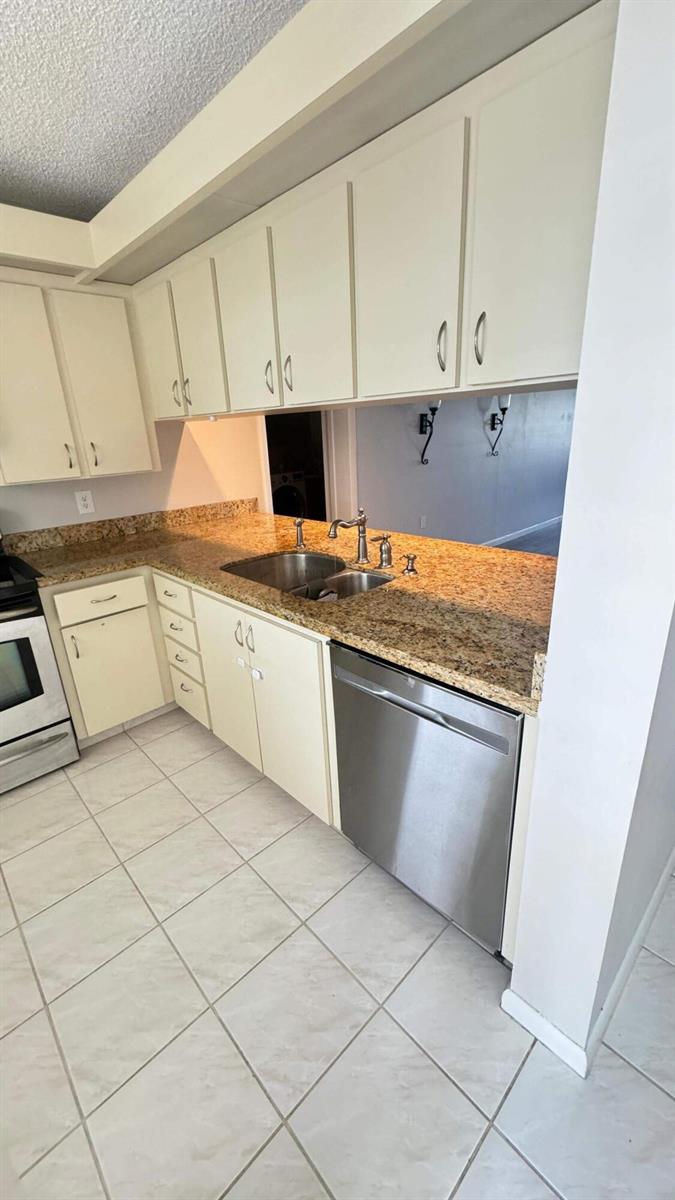A kitchen features cream-colored cabinets, granite countertops, stainless steel appliances, and light-colored tile flooring — 6049 Balboa Circle # 202, Boca Raton FL 33433, BOCA RATON, FL