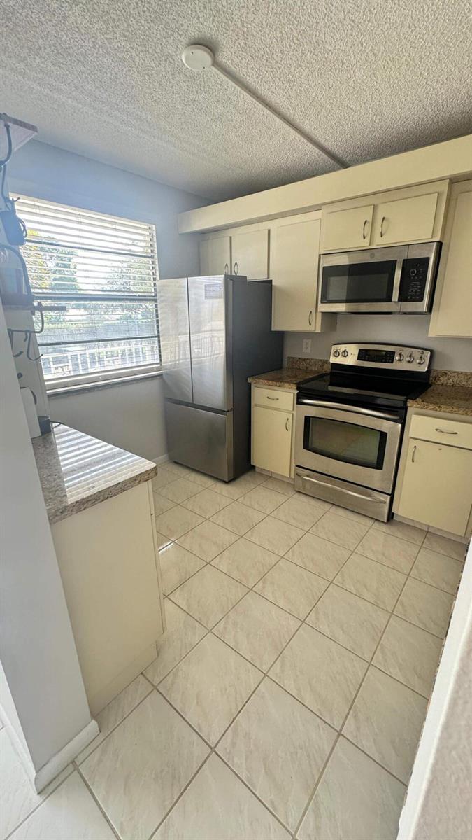 A kitchen features beige cabinets, stainless steel appliances, granite countertops, and light-colored tile flooring — 6049 Balboa Circle # 202, Boca Raton FL 33433, BOCA RATON, FL