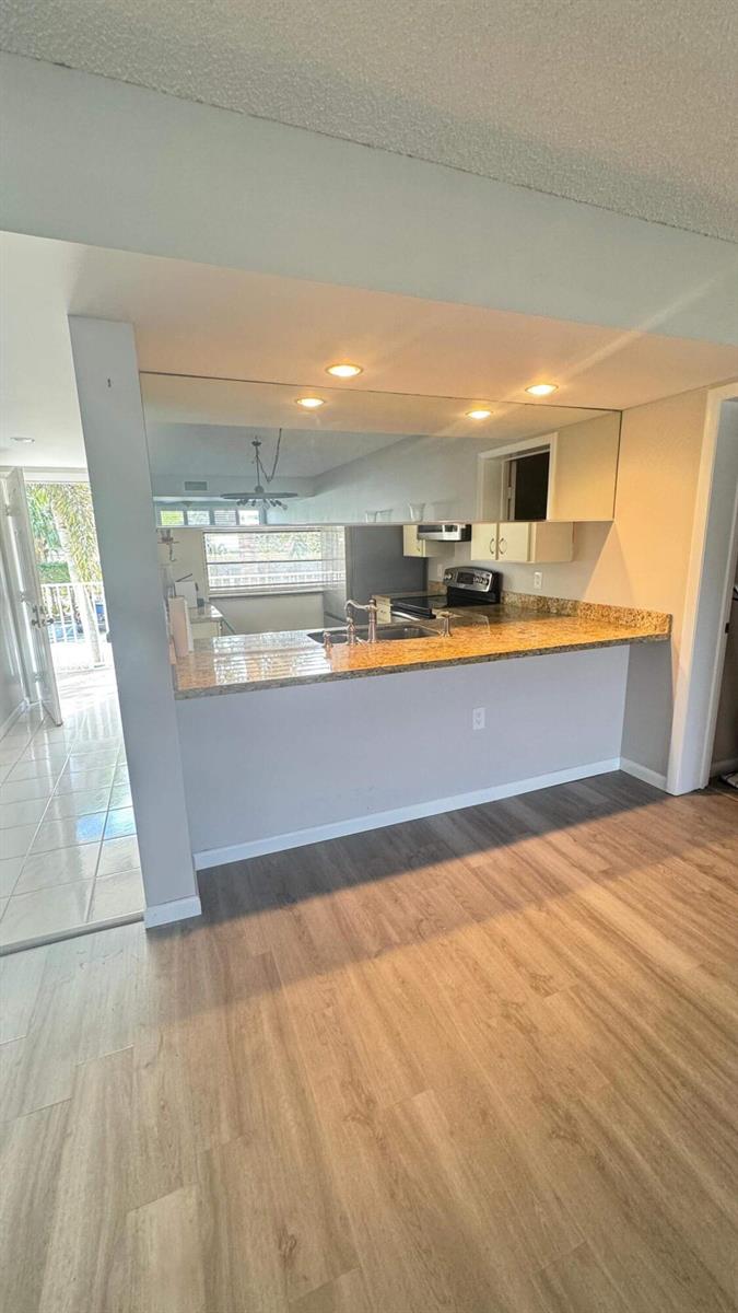 A kitchen with a granite breakfast bar, mirrored backsplash, and light wood-look flooring — 6049 Balboa Circle # 202, Boca Raton FL 33433, BOCA RATON, FL