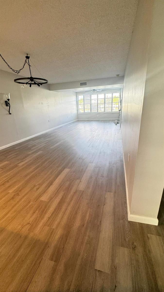 An empty living room features light wood-look flooring, gray walls, and a large window — 6049 Balboa Circle # 202, Boca Raton FL 33433, BOCA RATON, FL