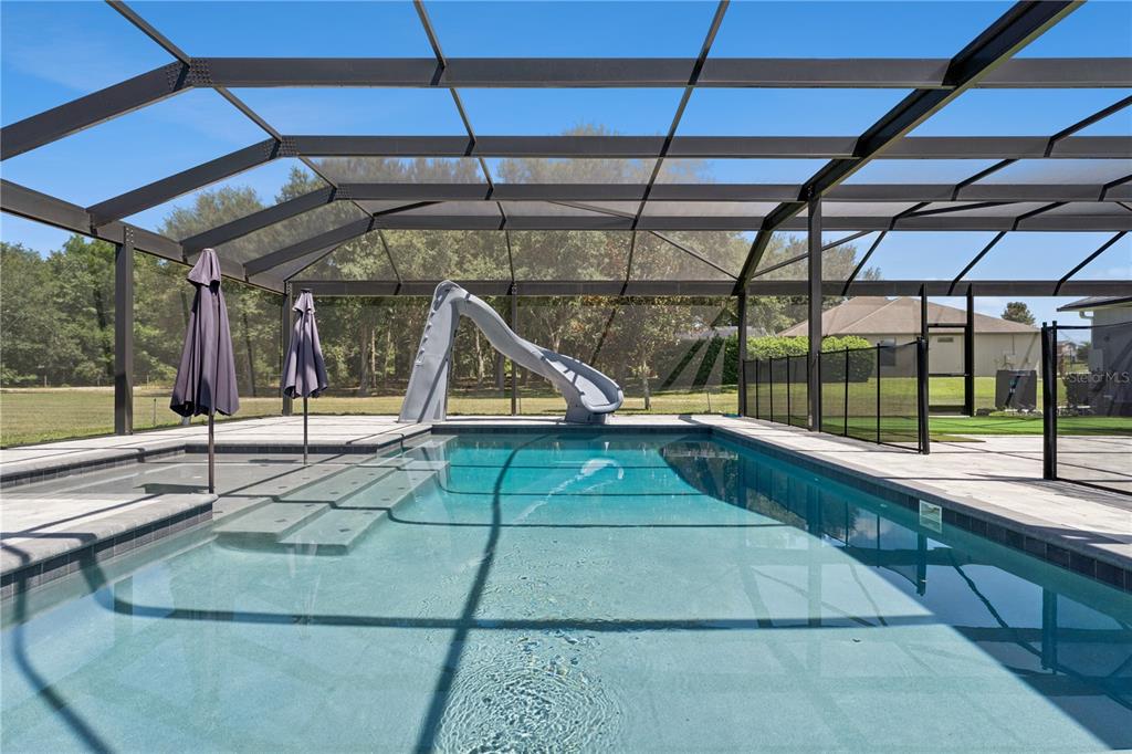 A swimming pool with a slide and umbrella is enclosed by a screened-in lanai — 18145 GREAT BLUE HERON DRIVE, GROVELAND, FL