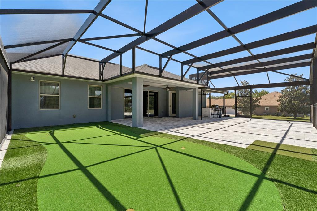 A screened-in patio features a putting green, paved flooring, and an outdoor bar area — 18145 GREAT BLUE HERON DRIVE, GROVELAND, FL
