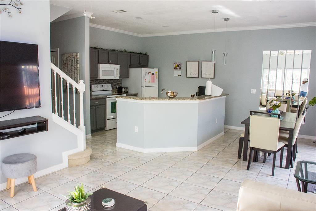 An open-concept kitchen with gray cabinets and a breakfast bar overlooks a dining area — 4720 VERO BEACH PLACE, KISSIMMEE, FL