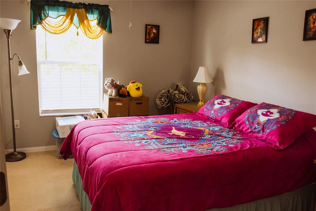 A bedroom features a bed with a bright pink patterned comforter and a window — 4720 VERO BEACH PLACE, KISSIMMEE, FL