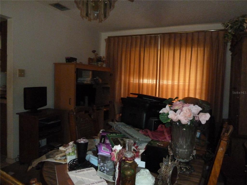 A dining room features a cluttered wooden table, a television stand, and floor-to-ceiling curtains — 16224 SAWGRASS CIRCLE, TAMPA, FL