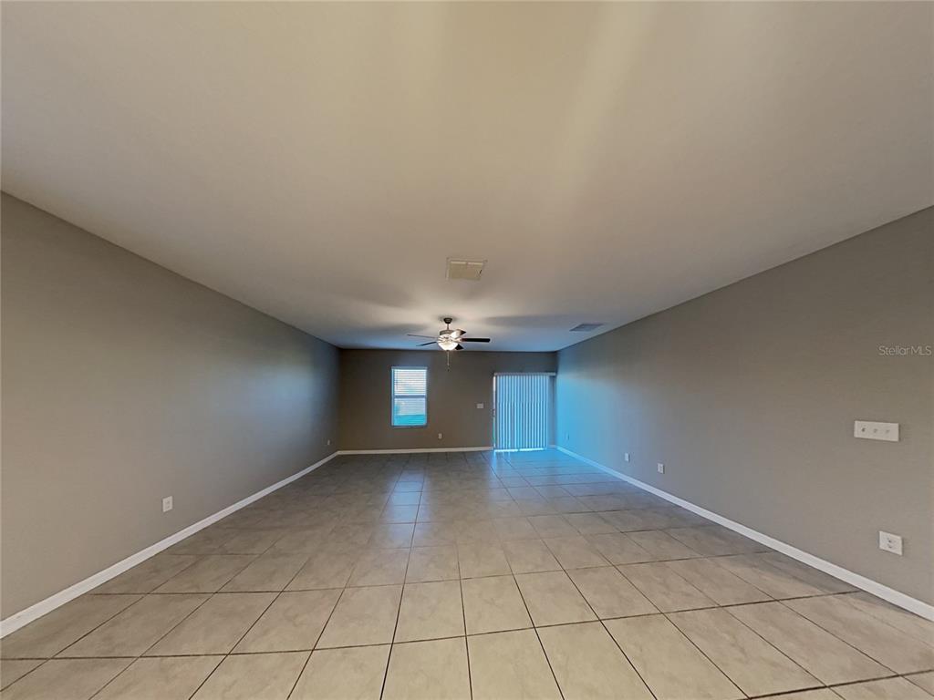 A spacious, empty room features gray walls, large light-colored floor tiles, and a ceiling fan — 4436 ETERNAL PRINCE DRIVE, SUN CITY CENTER, FL
