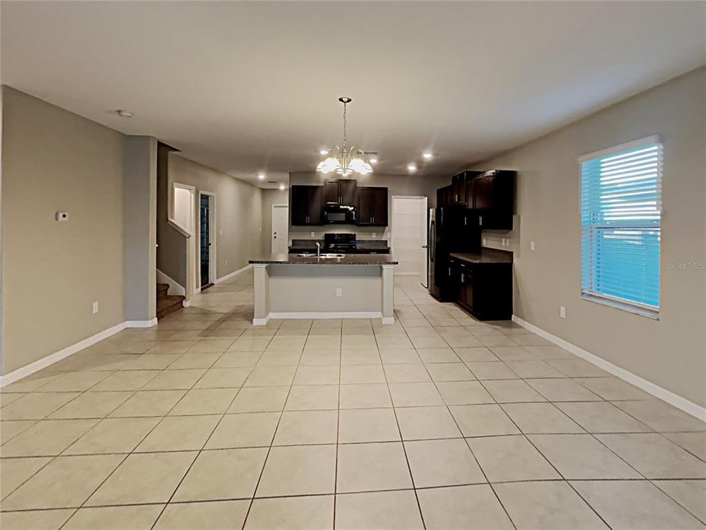 An open-concept kitchen features dark wood cabinets, a central island, and light-colored tile flooring — 4436 ETERNAL PRINCE DRIVE, SUN CITY CENTER, FL
