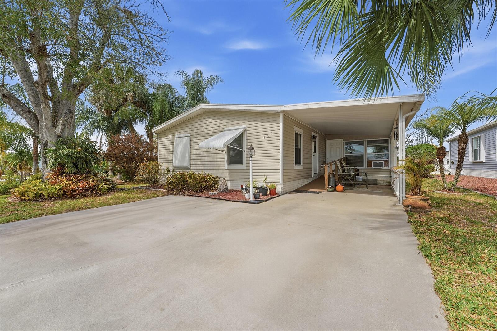 A single-story manufactured home with a concrete driveway, carport, and mature landscaping — 566 Dolphin Circle, Barefoot Bay FL 32976, BAREFOOT BAY, FL