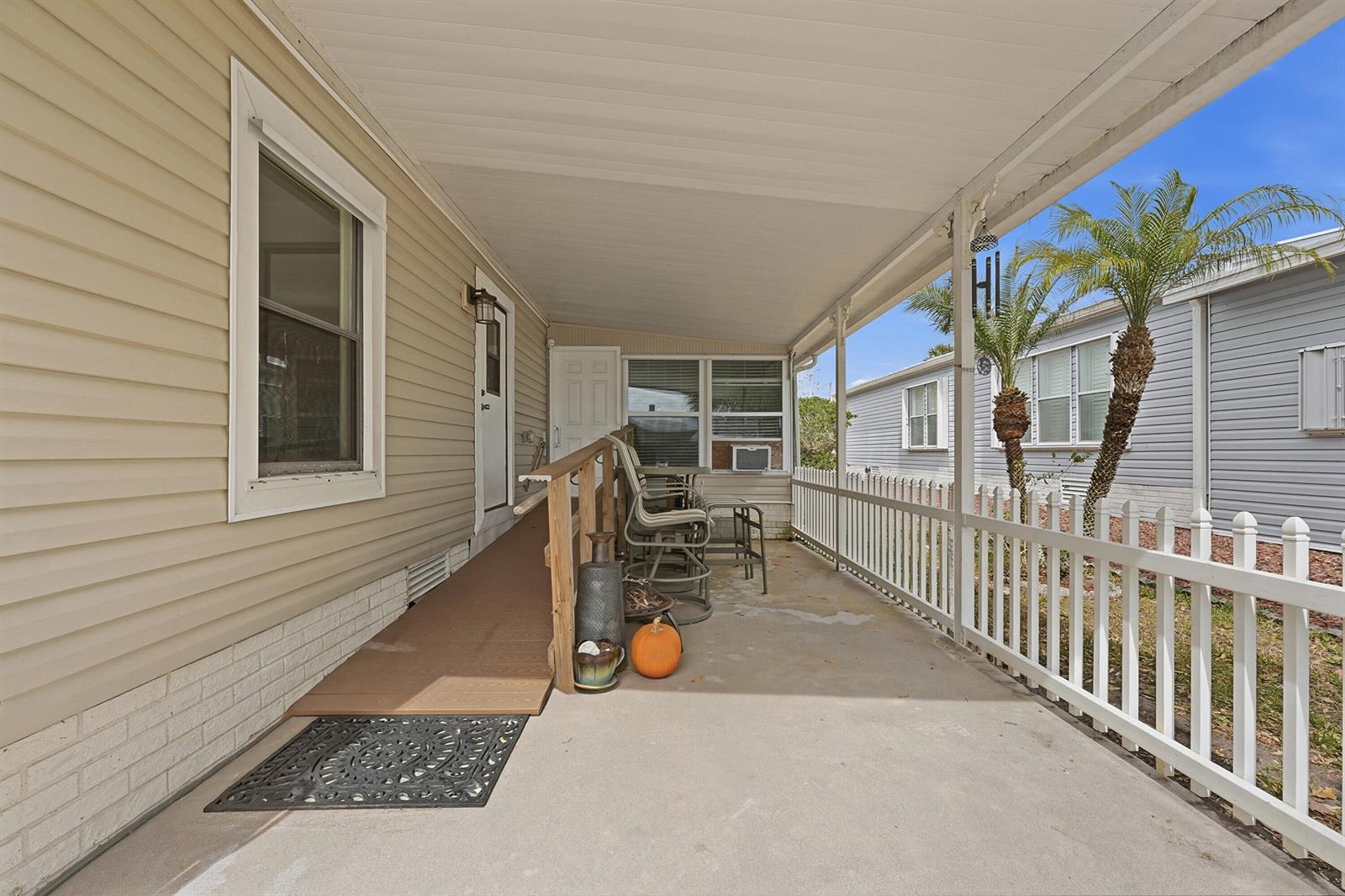 A covered concrete porch features a wooden ramp, white picket railing, and outdoor seating — 566 Dolphin Circle, Barefoot Bay FL 32976, BAREFOOT BAY, FL
