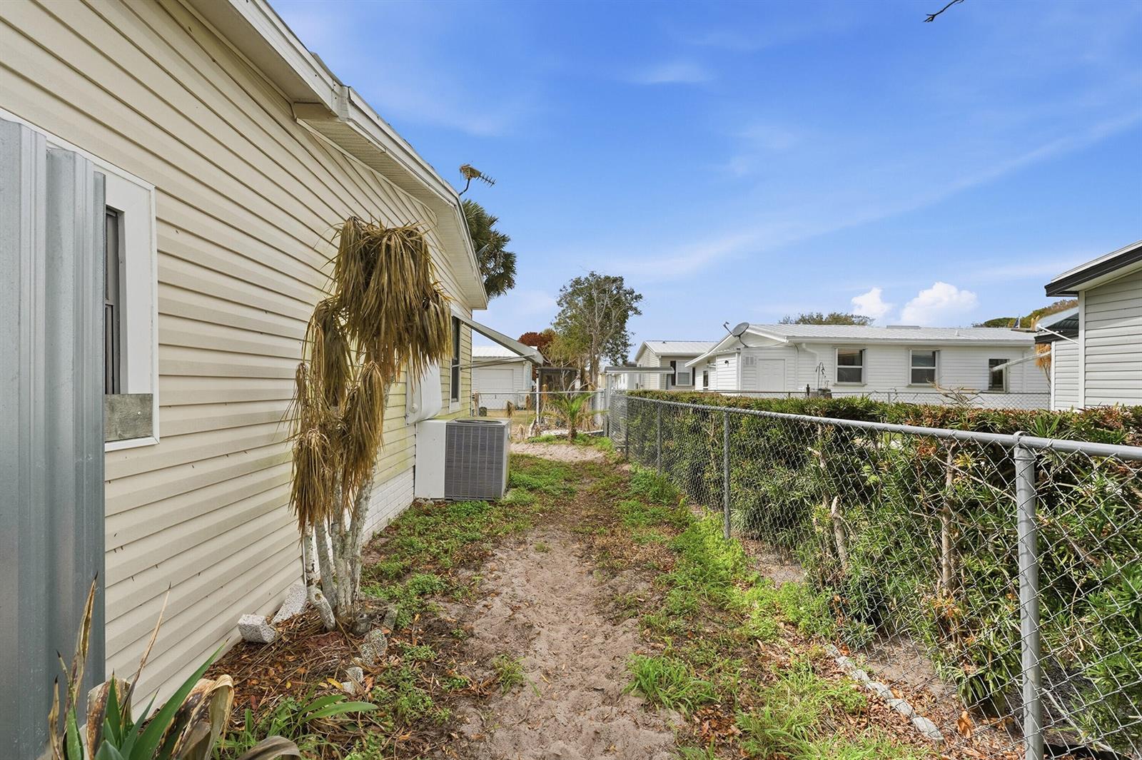 A narrow sandy side yard runs between a beige house and a chain-link fence — 566 Dolphin Circle, Barefoot Bay FL 32976, BAREFOOT BAY, FL