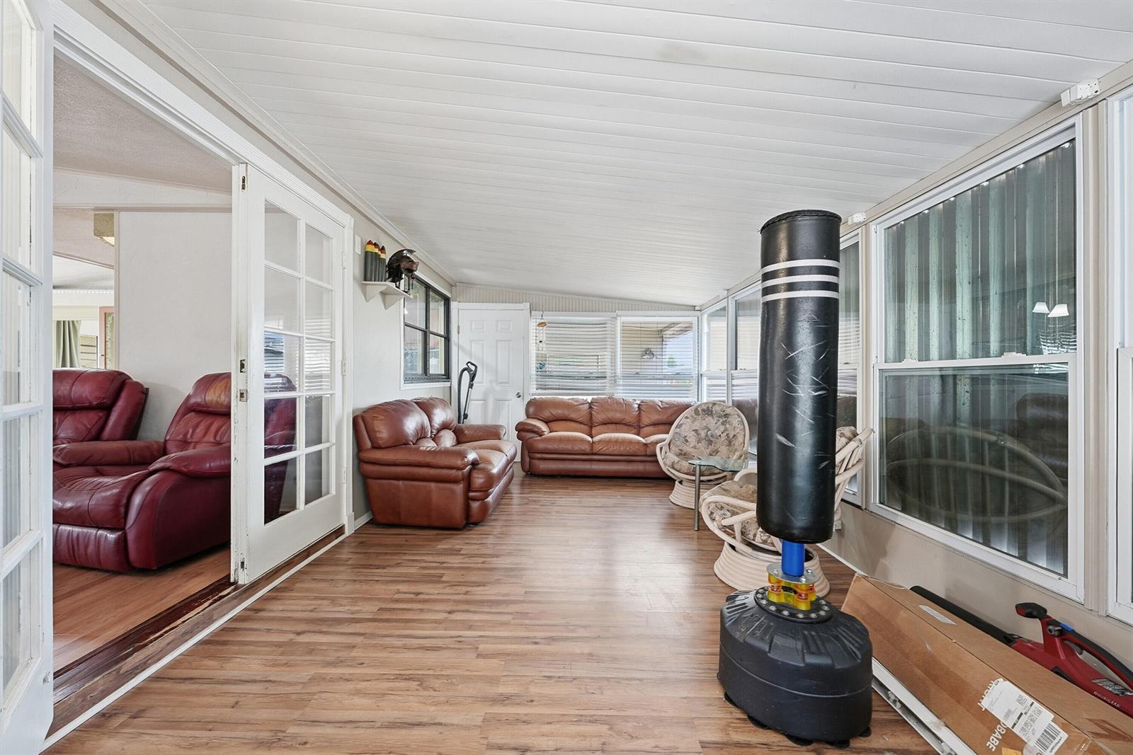 A sunroom features wood-look flooring, a punching bag, and two brown leather sofas — 566 Dolphin Circle, Barefoot Bay FL 32976, BAREFOOT BAY, FL