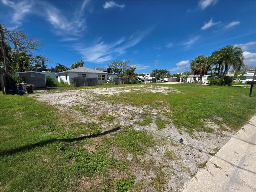 A vacant, grassy lot with a gravel driveway area and a small shed in the background — 14268 N BAYSHORE DRIVE, MADEIRA BEACH, FL