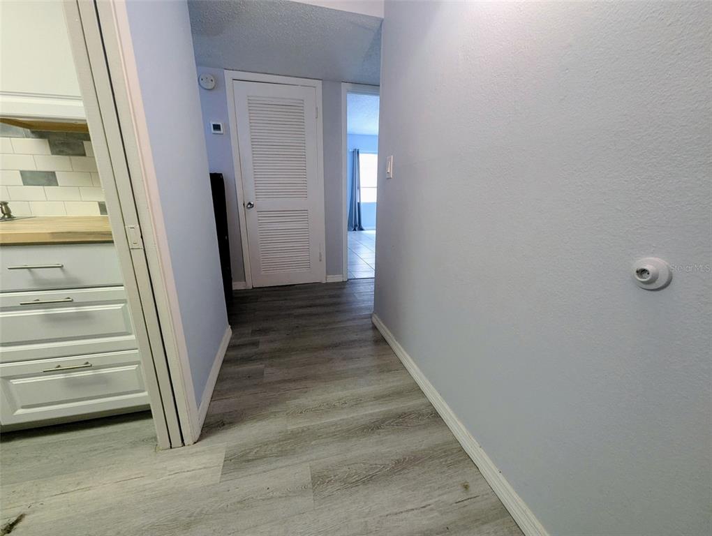 A hallway with light gray walls and wood-look flooring leads to a louvered door — 2366 E MALL DRIVE UNIT 313, FORT MYERS, FL