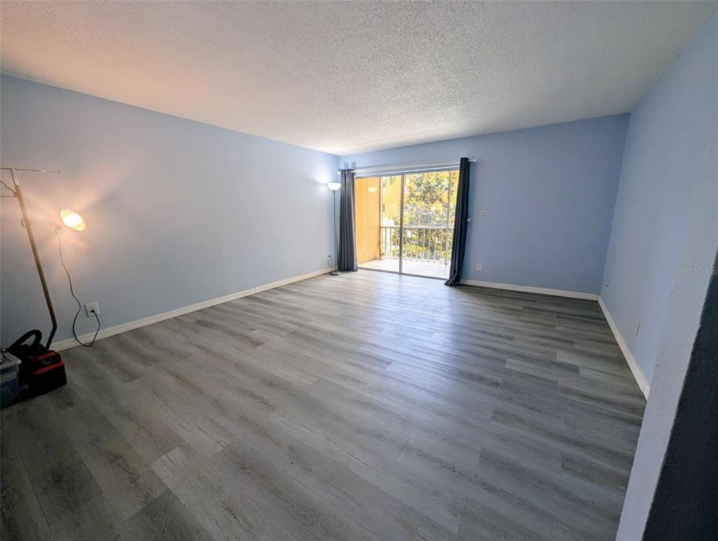 An empty living room features light blue walls, wood-look flooring, and a sliding glass balcony door — 2366 E MALL DRIVE UNIT 313, FORT MYERS, FL