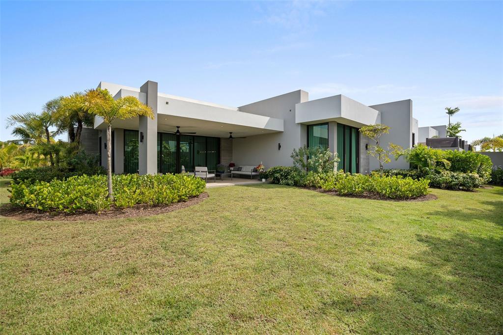 A modern, single-story house features a covered patio, large glass doors, and a landscaped lawn — 63 THE ISLES AT DORADO BEACH, DORADO, PR
