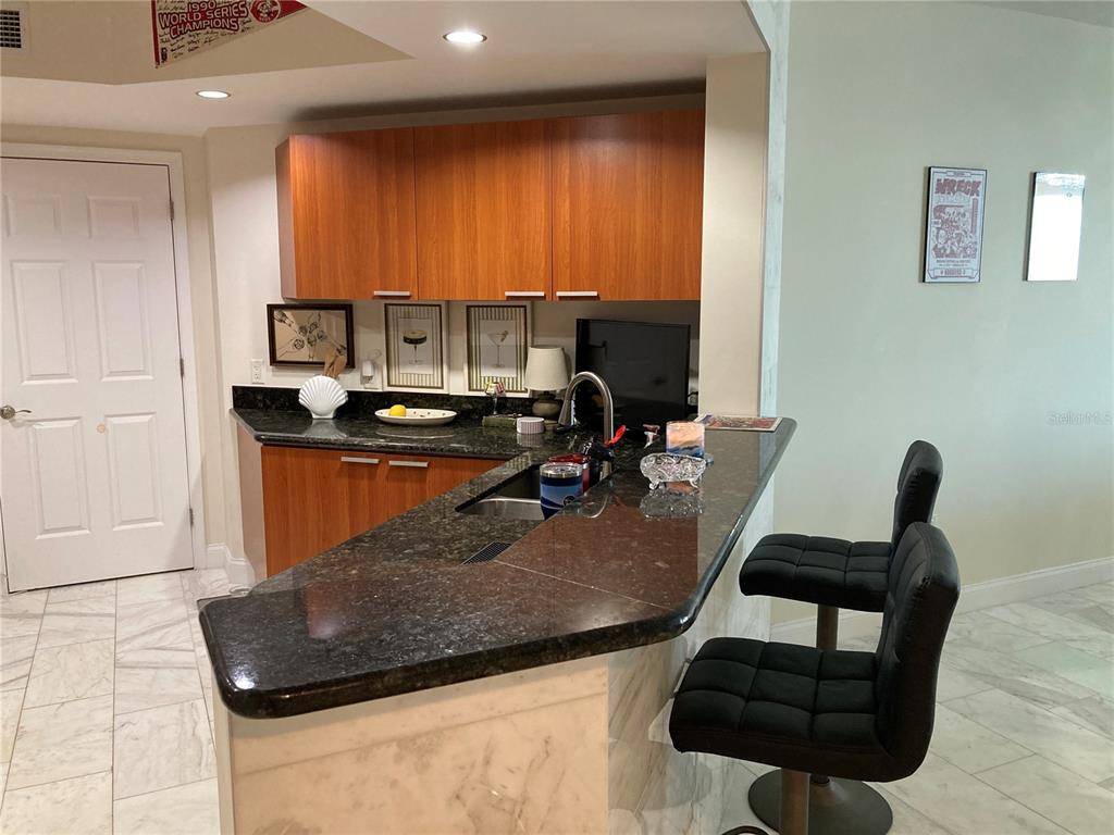 A kitchen features wood cabinets, dark granite countertops, a breakfast bar, and two black stools — 231 RIVERSIDE DRIVE UNIT 1504-1, DAYTONA BEACH, FL