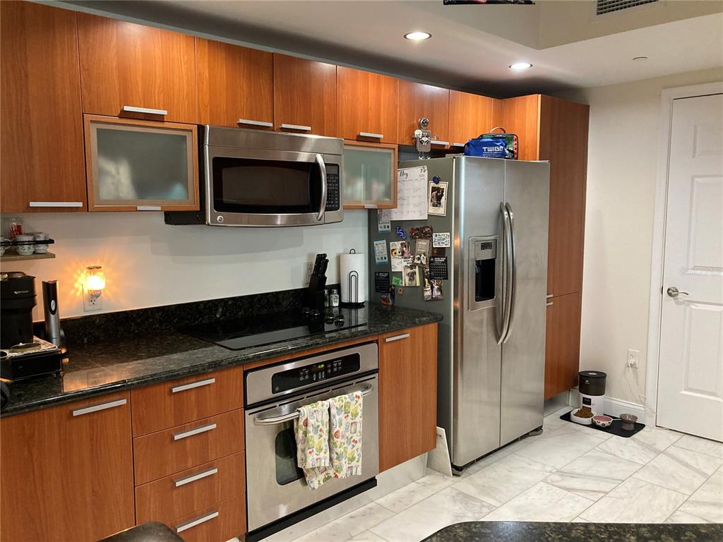 A kitchen features wood cabinets, stainless steel appliances, dark countertops, and light-colored tile flooring — 231 RIVERSIDE DRIVE UNIT 1504-1, DAYTONA BEACH, FL
